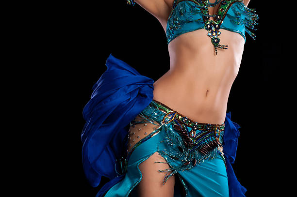 Torso of a female belly dancer wearing a teal blue costume and shaking her hips. Isolated on a black background.